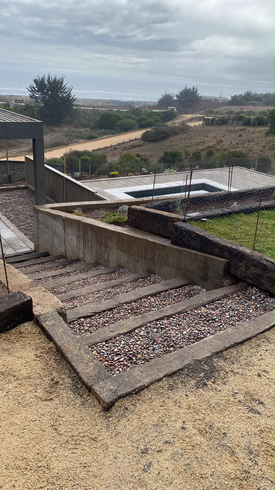 Escalera de durmientes con piedra de río y muro de contención mirando al mar