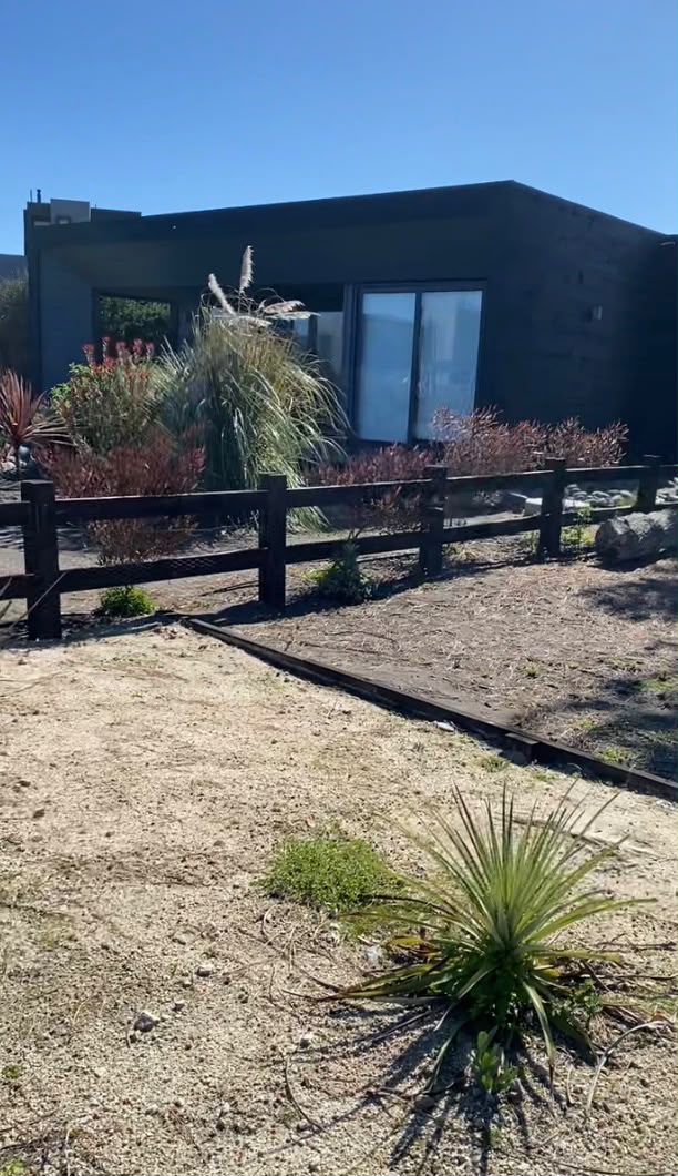 Jardín en arena con cerco de madera y plantaciones frente a la casa