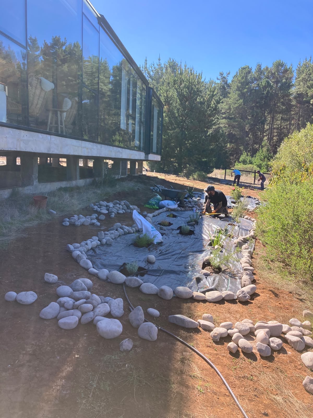 Instalación de un jardín de piedra de río junto a una casa de vidrio