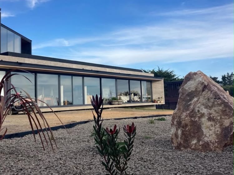 Jardín de gravilla con roca de granito frente a una casa contemporánea
