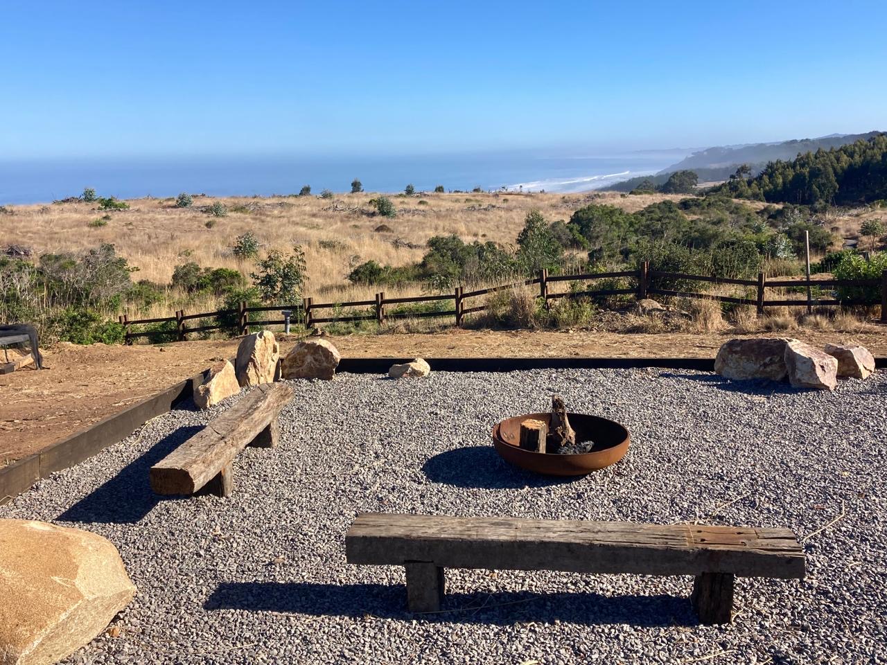 Zona de fogón con bancas de durmientes y piso de gravilla mirando al mar